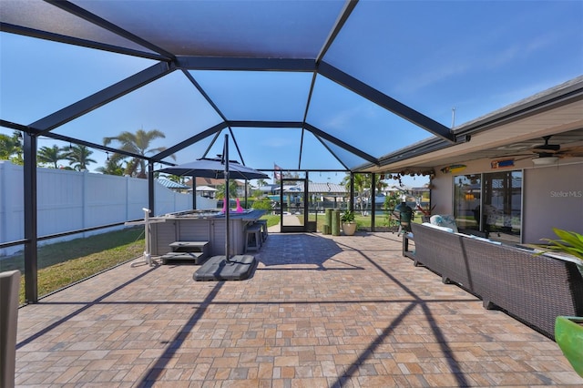 view of patio / terrace with glass enclosure, ceiling fan, fence, and a hot tub
