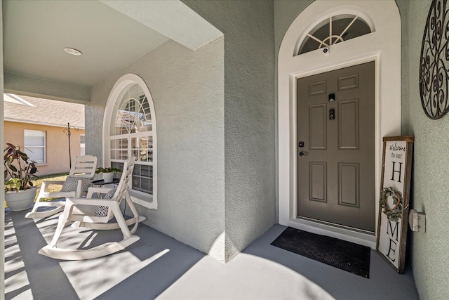 view of exterior entry featuring a porch and stucco siding