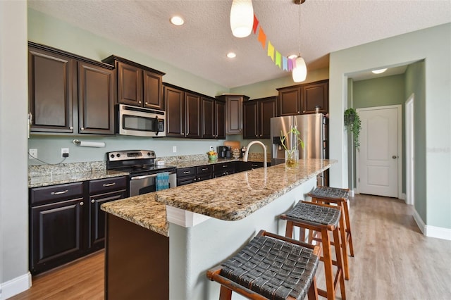 kitchen with dark brown cabinetry, light wood-style flooring, a kitchen breakfast bar, hanging light fixtures, and stainless steel appliances