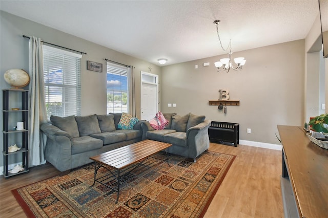 living room with baseboards, a textured ceiling, light wood-type flooring, and a notable chandelier