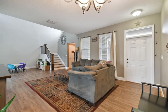 living area featuring light wood finished floors, baseboards, visible vents, stairs, and a chandelier