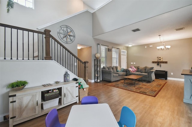 living area with visible vents, stairway, a towering ceiling, wood finished floors, and a chandelier