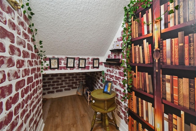 wine room with lofted ceiling, brick wall, a textured ceiling, and wood finished floors