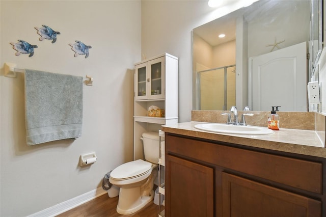 bathroom with toilet, vanity, a shower stall, wood finished floors, and baseboards