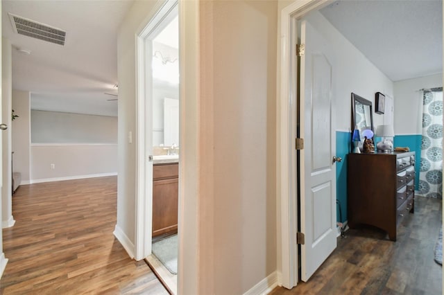 hall featuring a sink, baseboards, visible vents, and wood finished floors