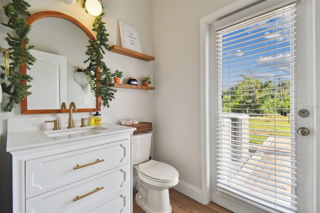 half bathroom featuring baseboards, vanity, toilet, and wood finished floors