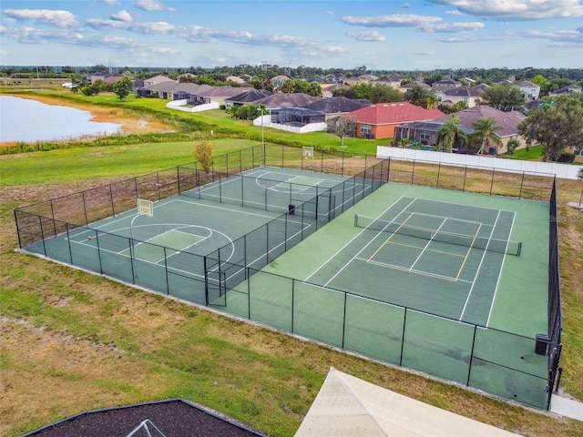 view of tennis court featuring a residential view, a water view, and fence