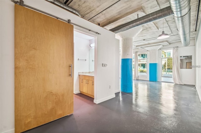 empty room with finished concrete flooring, a barn door, and baseboards