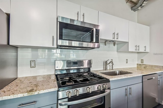 kitchen featuring appliances with stainless steel finishes, a sink, decorative backsplash, and light stone countertops