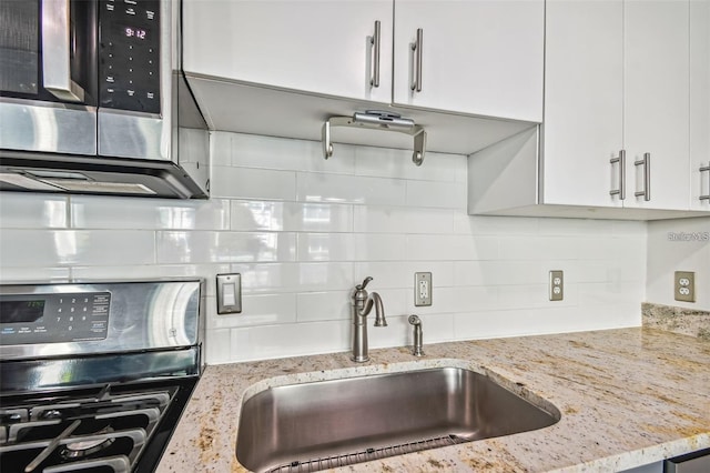 kitchen with tasteful backsplash, a sink, stainless steel range with gas stovetop, and white cabinetry