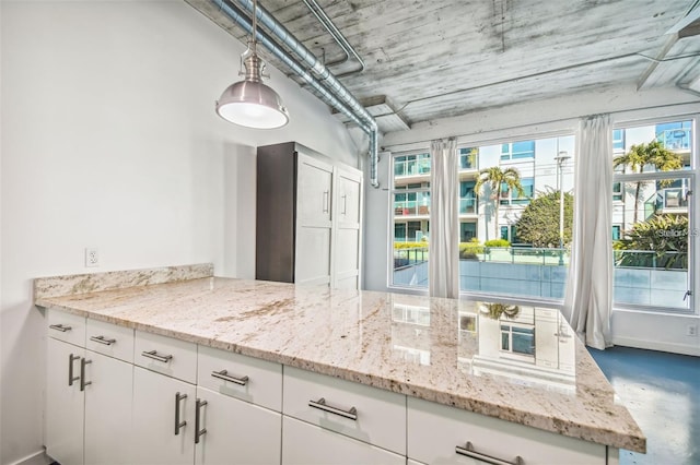 kitchen with light stone counters, white cabinets, concrete flooring, and baseboards