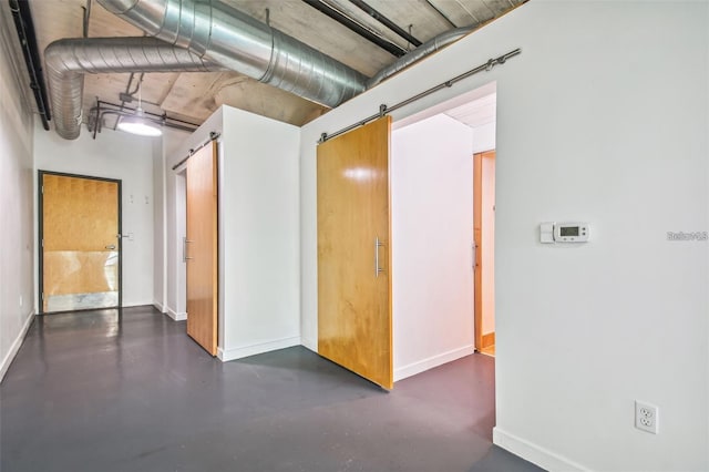 spare room with a barn door, concrete floors, and baseboards