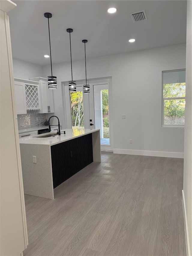 kitchen featuring a center island with sink, visible vents, light wood-type flooring, a sink, and tasteful backsplash