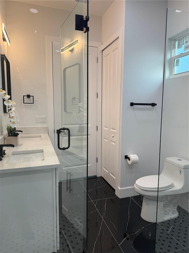 full bath featuring baseboards, toilet, double vanity, a stall shower, and a sink