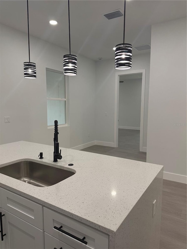 kitchen featuring pendant lighting, light stone counters, visible vents, and a sink