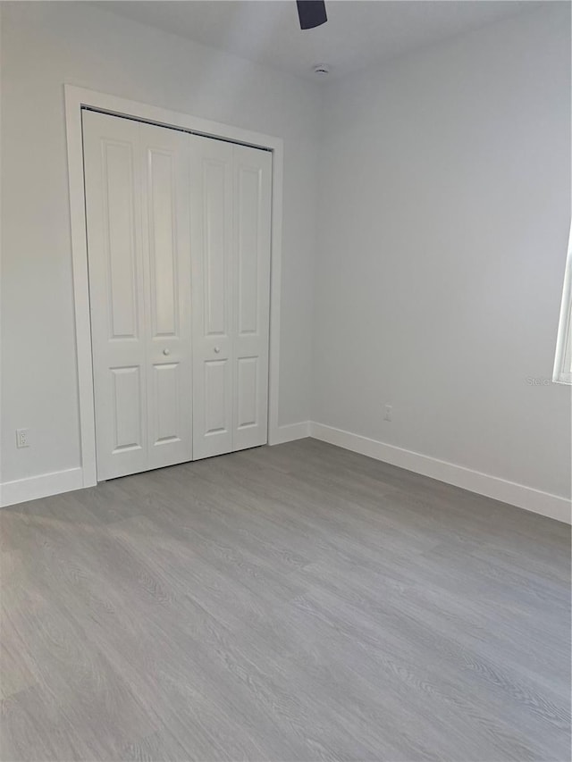 unfurnished bedroom with a closet, baseboards, dark wood-type flooring, and ceiling fan