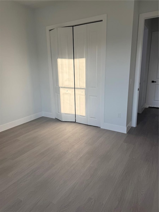 unfurnished bedroom featuring dark wood-style floors, a closet, and baseboards