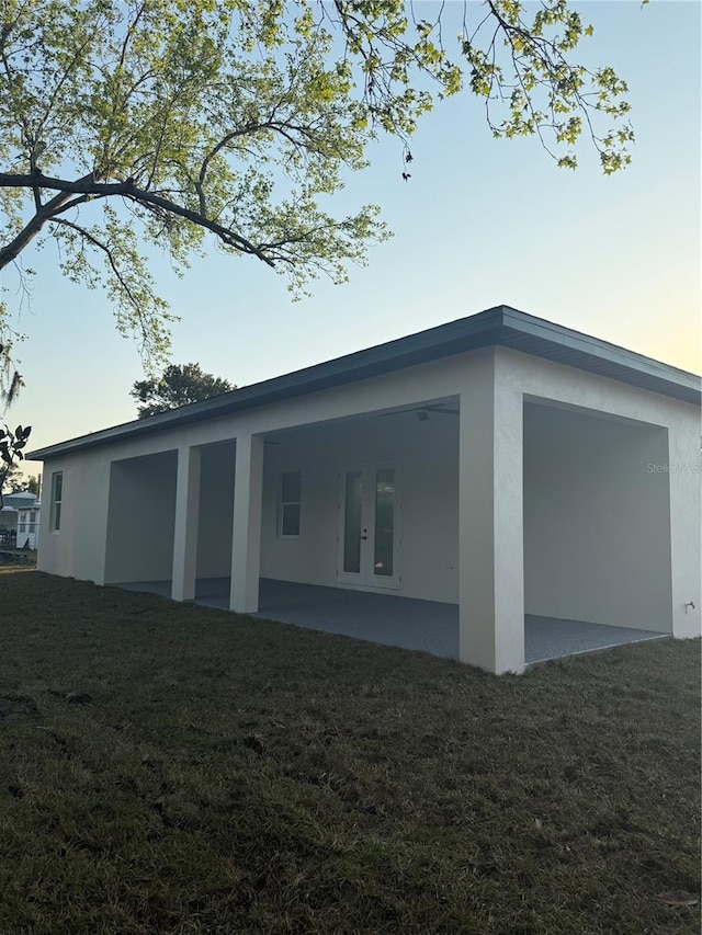 view of property exterior with a patio area, french doors, a lawn, and stucco siding