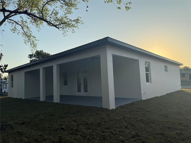 property exterior at dusk featuring a patio, a lawn, french doors, and stucco siding