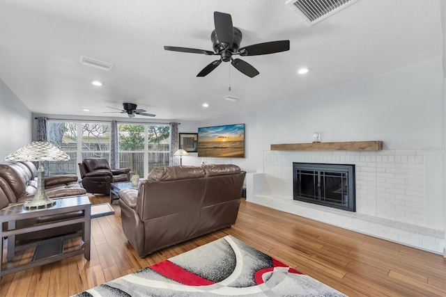 living area with a brick fireplace, visible vents, and wood finished floors