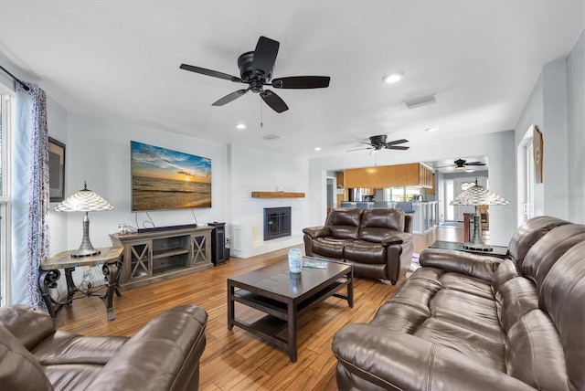 living room featuring a glass covered fireplace, visible vents, recessed lighting, and wood finished floors