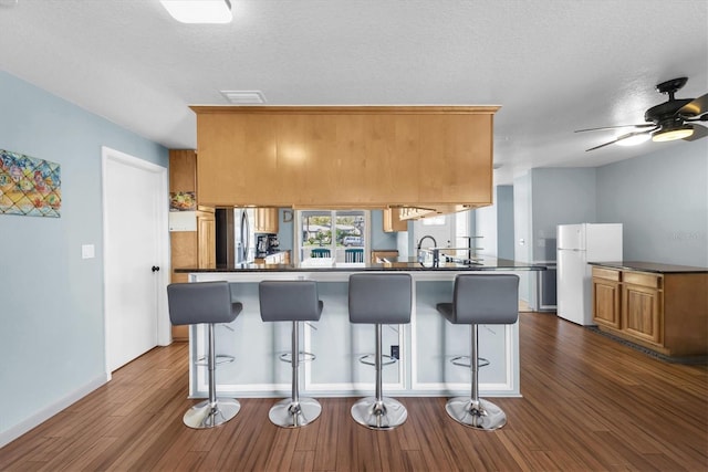 kitchen featuring a peninsula, a kitchen breakfast bar, freestanding refrigerator, dark wood-style floors, and dark countertops