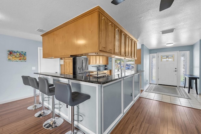 kitchen featuring stainless steel refrigerator with ice dispenser, visible vents, dark wood-type flooring, a sink, and a textured ceiling