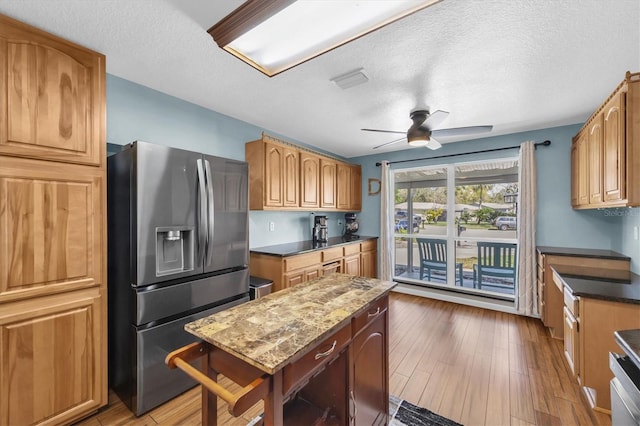 kitchen featuring appliances with stainless steel finishes, a ceiling fan, a textured ceiling, dark stone countertops, and wood finished floors