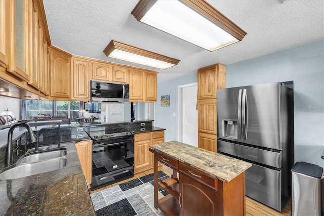 kitchen featuring stainless steel appliances, dark stone counters, a sink, and a kitchen island