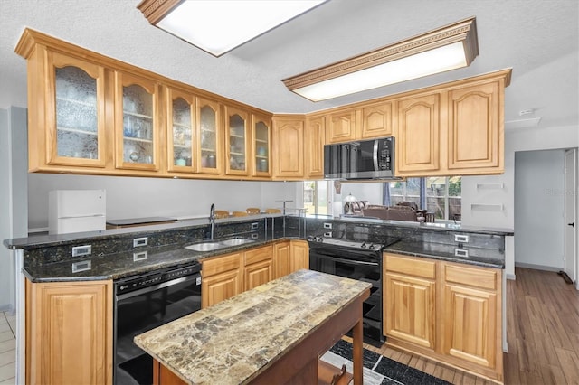 kitchen with a peninsula, a sink, dark stone counters, black appliances, and glass insert cabinets