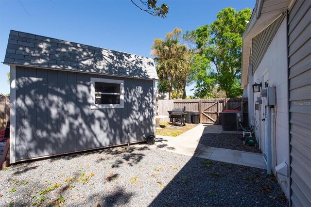 view of side of home featuring central AC unit, a fenced backyard, an outdoor structure, roof with shingles, and a storage unit