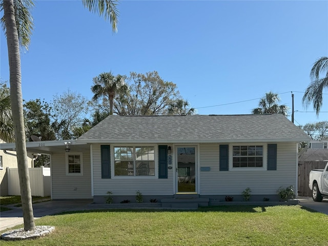 ranch-style home with fence, a front lawn, a carport, and roof with shingles