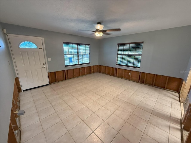 entryway featuring a textured ceiling, wood walls, wainscoting, and a ceiling fan