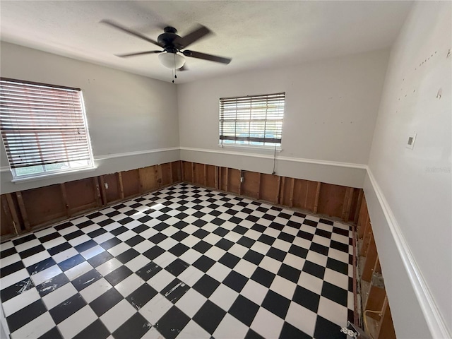 spare room featuring a ceiling fan, a wainscoted wall, wood walls, and tile patterned floors