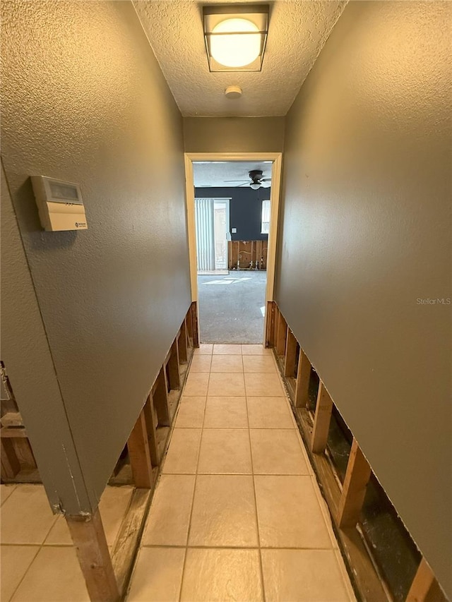 hallway featuring light carpet, light tile patterned floors, a textured ceiling, and a textured wall