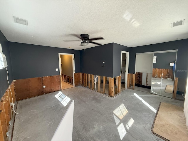 unfurnished living room featuring a ceiling fan, visible vents, and a textured ceiling