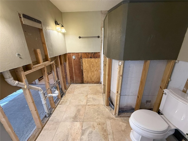 bathroom with a wainscoted wall, stone finish floor, and toilet