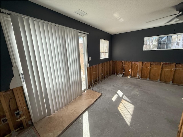 empty room with ceiling fan, visible vents, a textured ceiling, and wainscoting