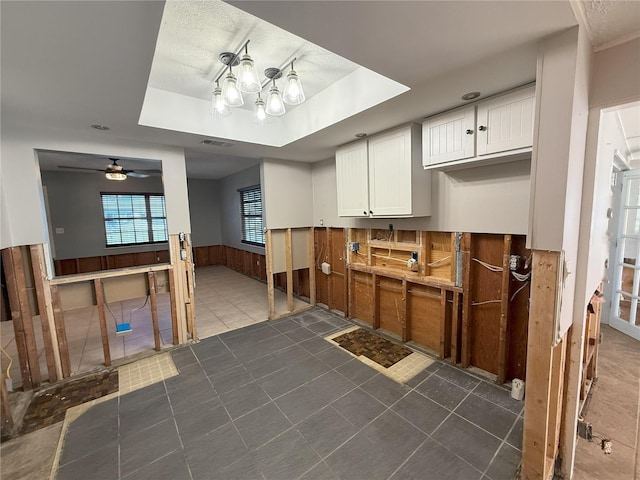 kitchen with wooden walls, visible vents, white cabinets, wainscoting, and a tray ceiling