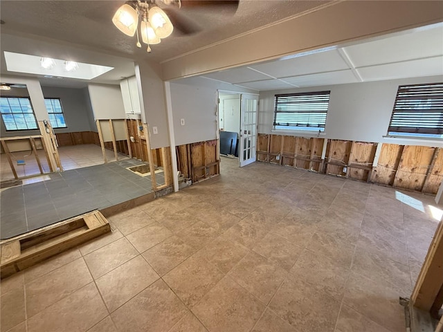 spare room featuring a healthy amount of sunlight, ceiling fan, wooden walls, and wainscoting