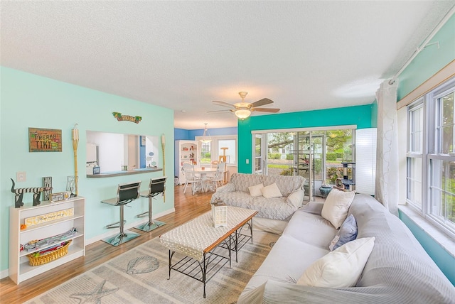 living room featuring ceiling fan, a textured ceiling, baseboards, and wood finished floors