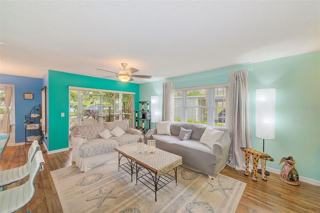 living room with a textured ceiling, ceiling fan, wood finished floors, and baseboards