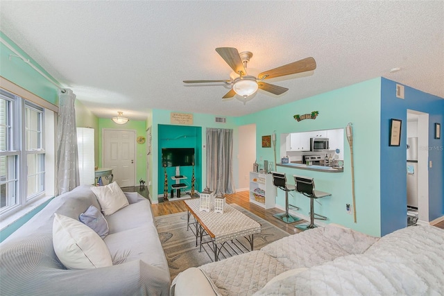 living area featuring ceiling fan, a textured ceiling, visible vents, and wood finished floors