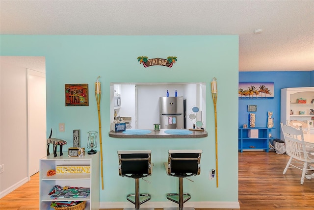 kitchen featuring freestanding refrigerator, a textured ceiling, a kitchen breakfast bar, wood finished floors, and baseboards