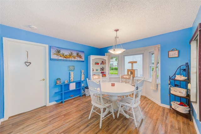 dining room with light wood-type flooring, a textured ceiling, and baseboards