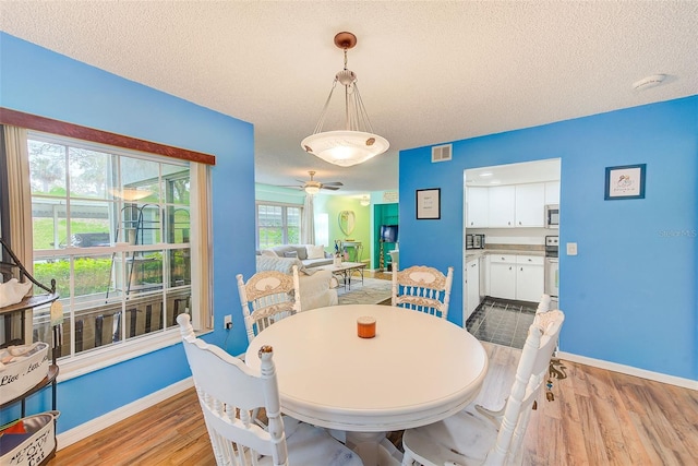 dining space with light wood-style floors, baseboards, visible vents, and a textured ceiling