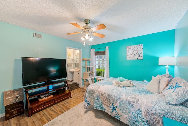 bedroom featuring ceiling fan, a textured ceiling, visible vents, and wood finished floors