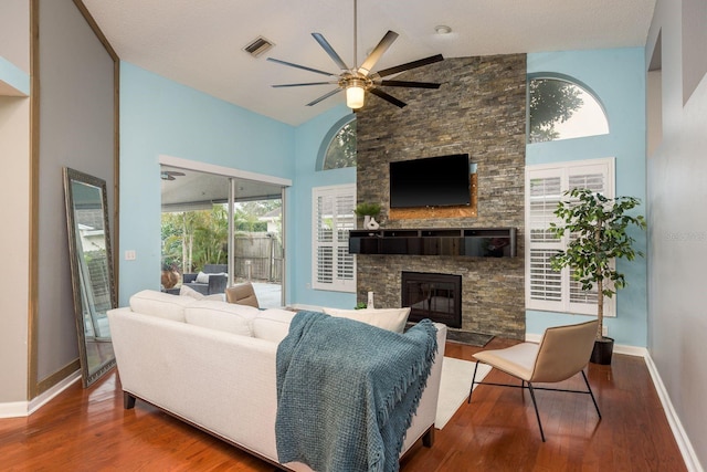 living area with high vaulted ceiling, visible vents, a stone fireplace, and wood finished floors