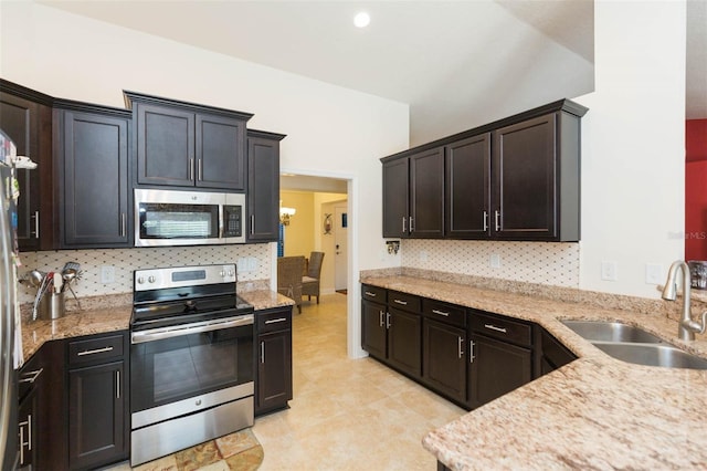 kitchen with stainless steel appliances, light stone counters, a sink, and decorative backsplash