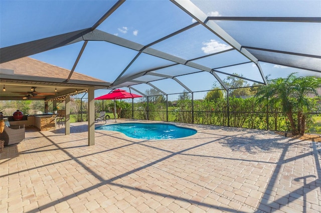outdoor pool featuring outdoor dry bar, glass enclosure, a patio area, and a ceiling fan